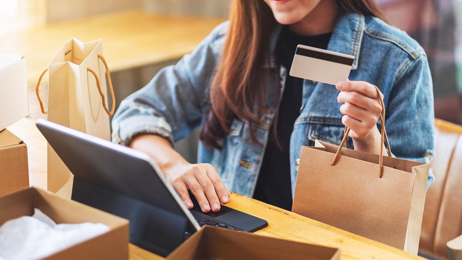 A shopper paying by card at a small eCommerce brand's counter surrounded by paper bags and a tablet.