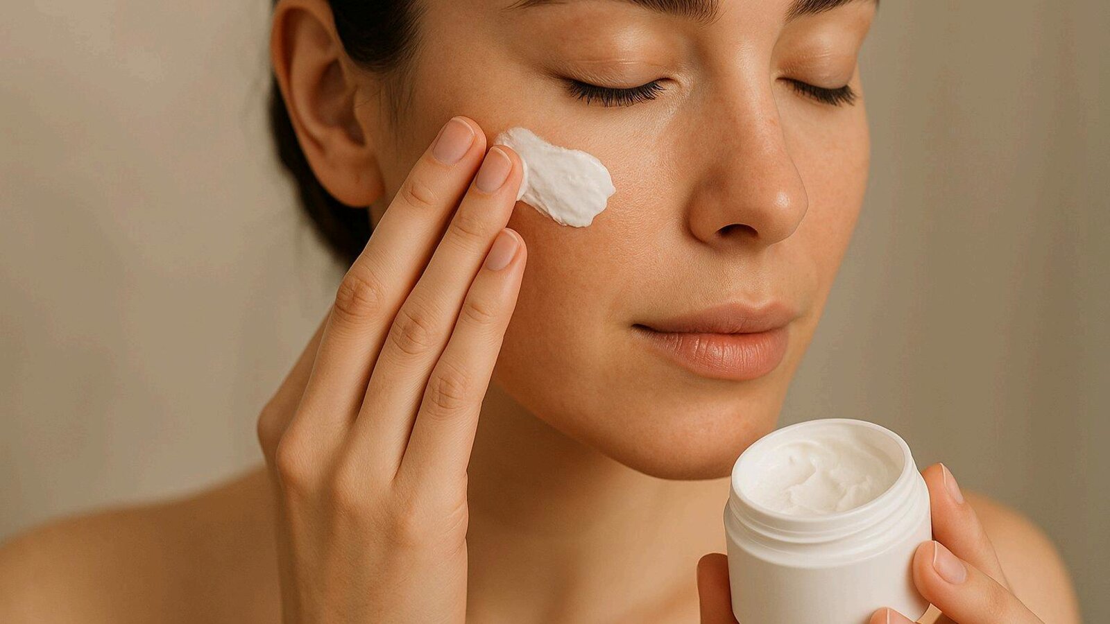 A woman applying a dab of luxury face cream, holding an open white jar of moisturizer.