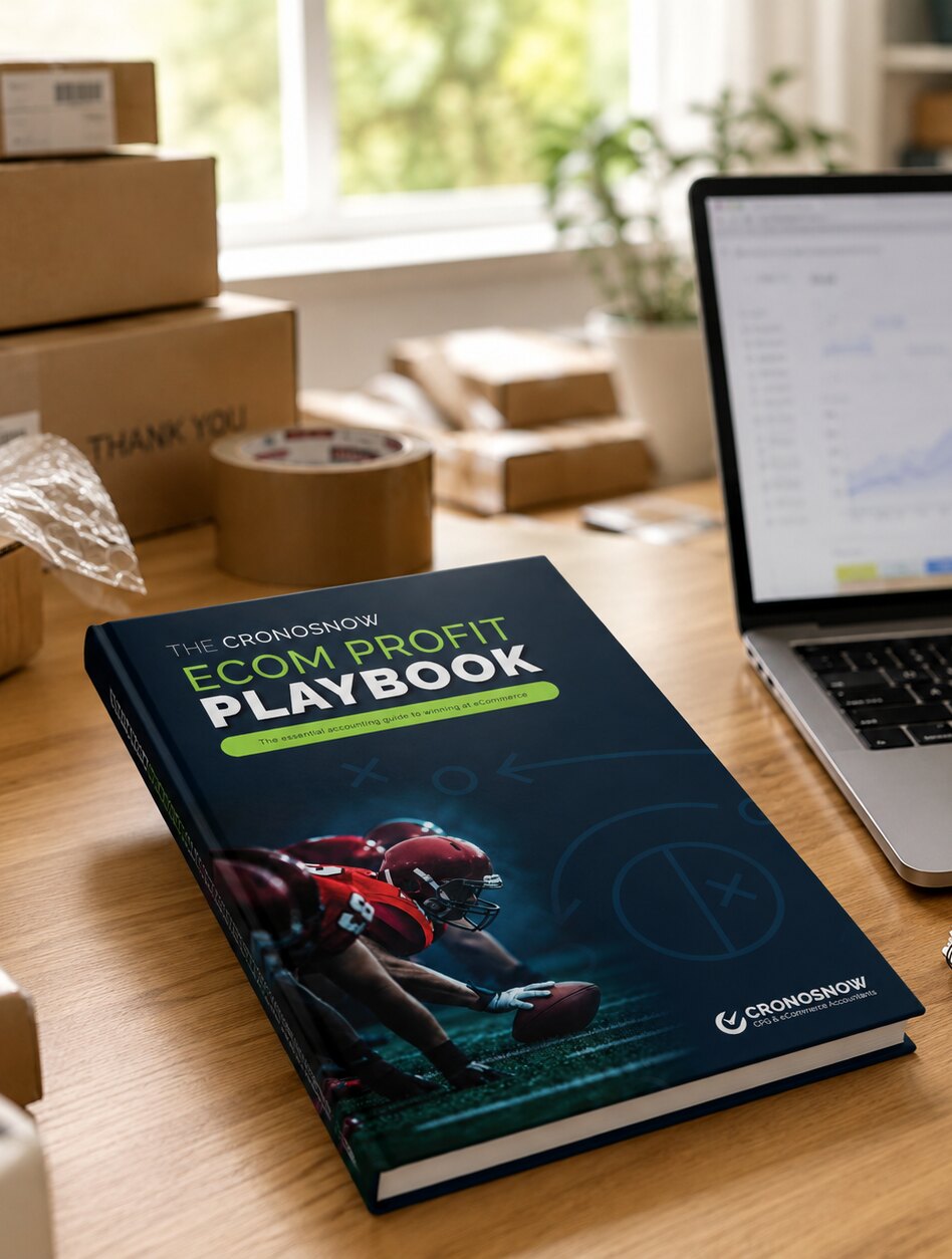 The eCom Profit Playbook on a seller&rsquo;s packing desk beside a laptop showing sales dashboards.
